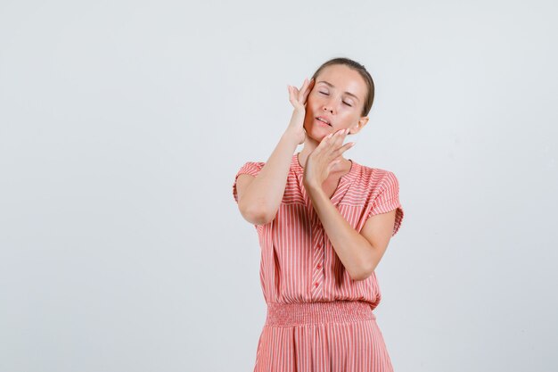 Young female in striped dress rubbing temples carefully and looking relaxed , front view.