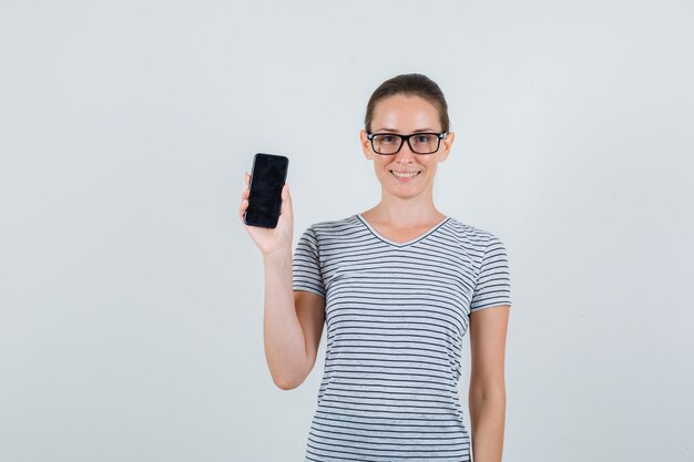 Young female in striped t-shirt, glasses holding mobile phone and looking glad , front view.