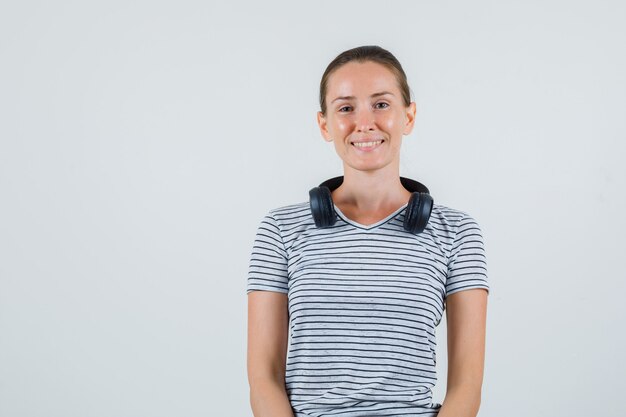 Young female in striped t-shirt, headphones and looking cheery , front view.