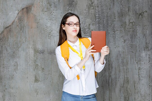 本を持って立っている眼鏡の若い女子学生。高品質の写真