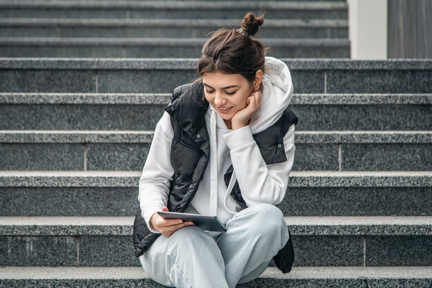 若い女子学生が外でデジタル タブレットを手に立っている