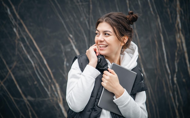 A young female student stands with a digital tablet in her hands outside