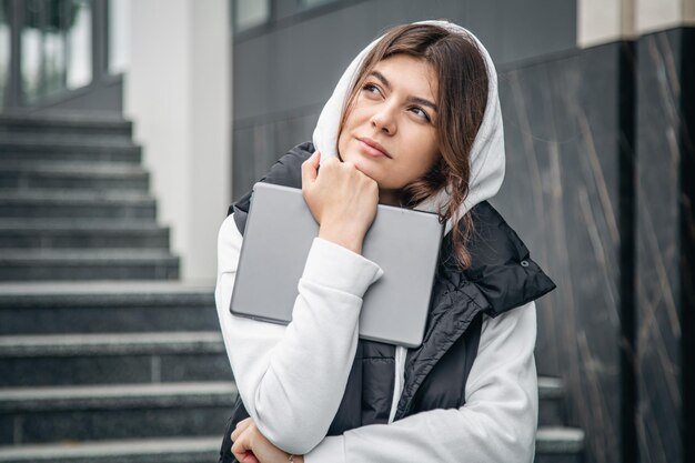 若い女子学生がデジタルタブレットを手に外に立つ