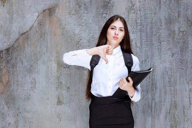 Young female student with backpack and books giving thumbs down. High quality photo