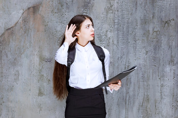 何かを聞こうとしているバックパックと本を持つ若い女子学生。高品質の写真