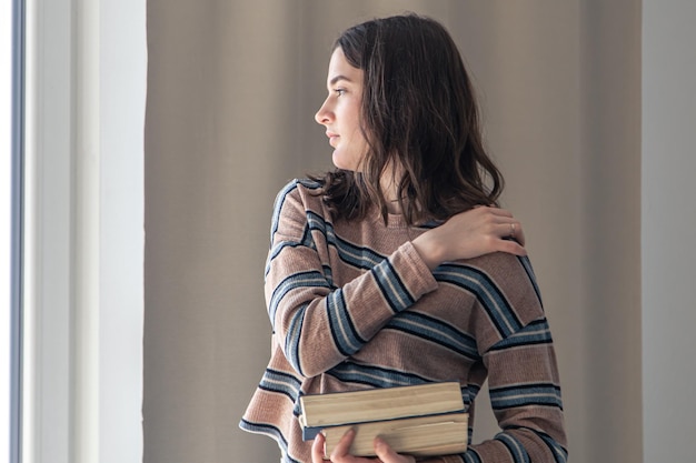 A young female student with books in her hands in the room