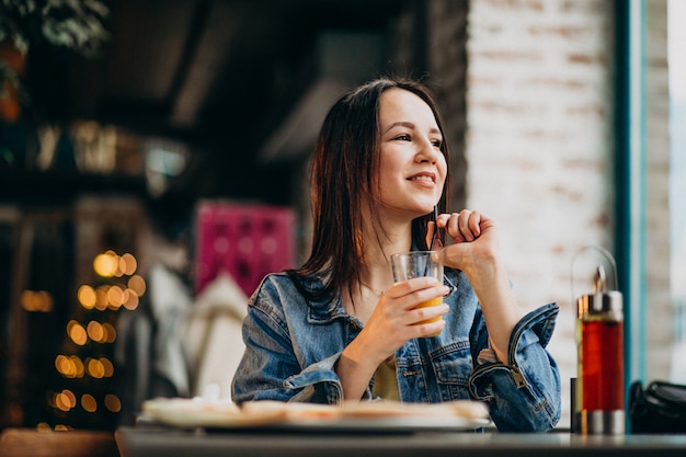 若い女子学生のラップトップに取り組んでバーでピザを食べる