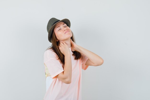 Young female suffering from neck pain in pink t-shirt, hat and looking uncomfortable , front view.