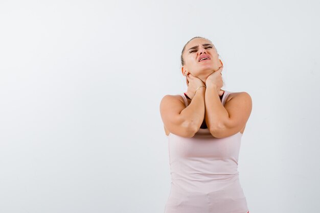 Young female suffering from neckache in singlet and looking unwell. front view.