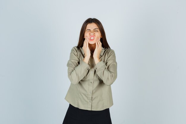 Young female suffering from painful toothache in shirt, skirt and looking uncomfortable