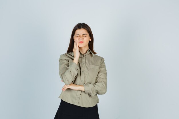 Young female suffering from toothache in shirt, skirt and looking painful