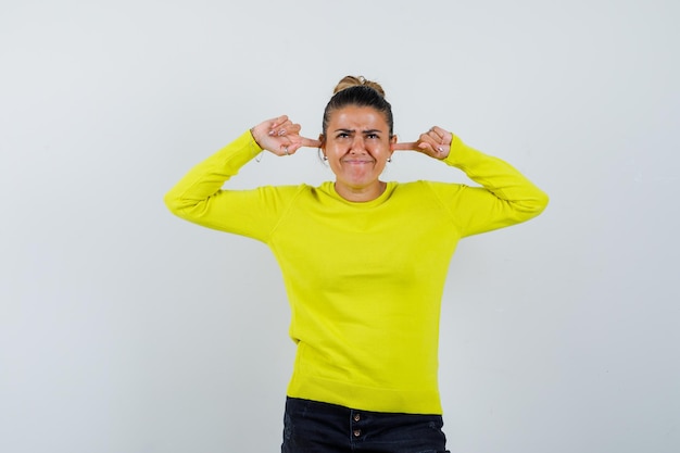 Young female in sweater, denim skirt plugging ears with fingers and looking confused 