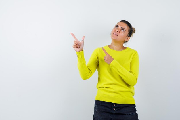 Young female in sweater, denim skirt pointing aside and looking focused 