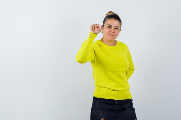 Young female in sweater, denim skirt pointing camera and looking joyful 