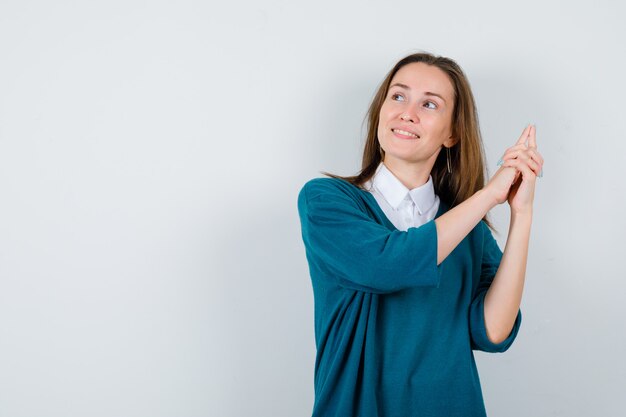 Young female in sweater over shirt showing gun gesture, looking away and looking jolly , front view.