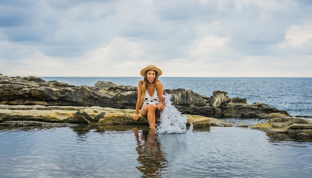 海の近くの岩の上に点が座っている水着の若い女性