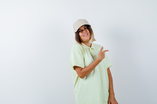 Young female in t-shirt, cap pointing away and looking happy , front view.