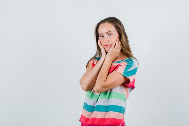 Молодая женщина в футболке, взявшись за руки на щеках, вид спереди.