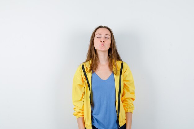 Young female in t-shirt, jacket keeping lips folded and looking pretty, front view.