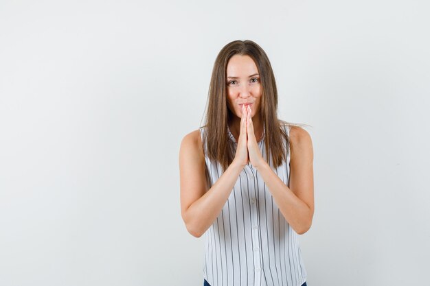 Young female in t-shirt, jeans bowing head and showing namaste gesture, front view.