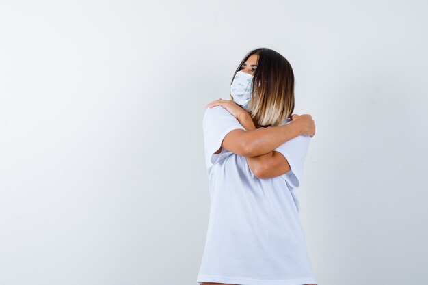 Young female in t-shirt, mask hugging herself and looking cute , front view.