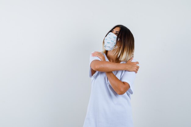 Young female in t-shirt, mask hugging herself and looking peaceful , front view.