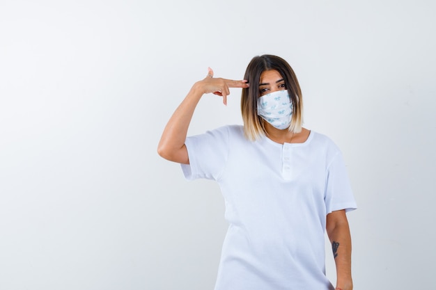Young female in t-shirt, mask making suicide gesture and looking hopeless , front view.