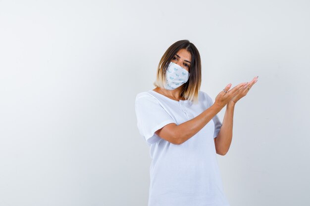 Young female in t-shirt, mask welcoming something and looking confident , front view.