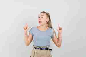 Free photo young female in t-shirt, pants pointing up and looking joyful , front view.