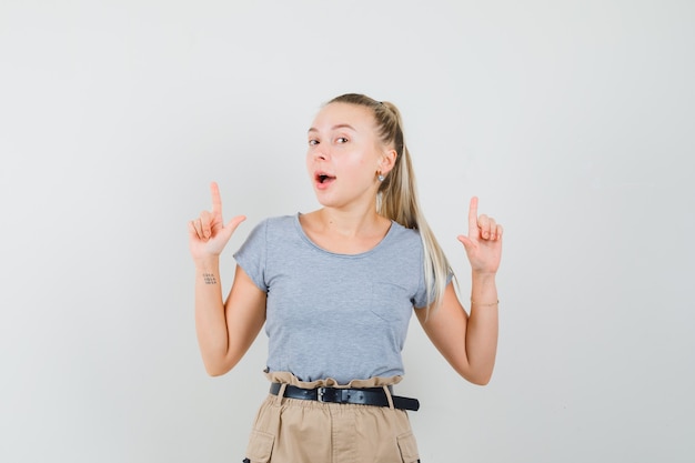 Young female in t-shirt, pants pointing up and looking joyful , front view.