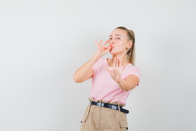 Foto gratuita giovane donna in t-shirt, pantaloni che mostrano un gesto delizioso e di rifiuto, vista frontale.