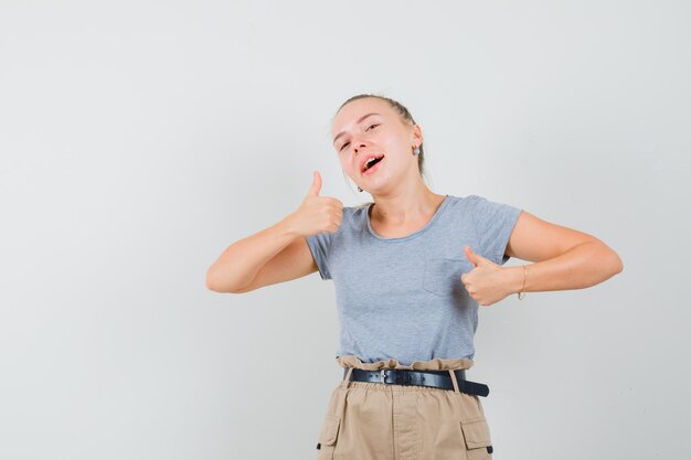 Young female in t-shirt, pants showing double thumbs up and looking merry , front view.