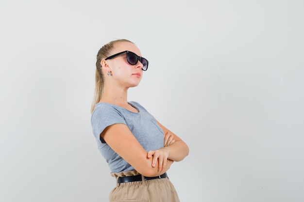 Young female in t-shirt, pants standing with crossed arms and looking confident , front view.