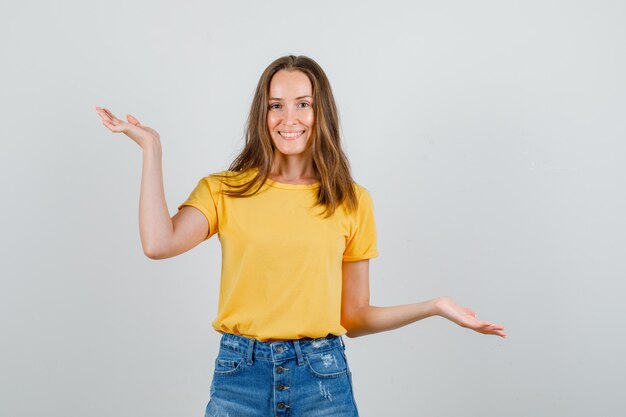 Young female in t-shirt, shorts holding open palms like scales and looking cheerful