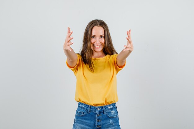 Young female in t-shirt, shorts inviting to come with hands and looking merry