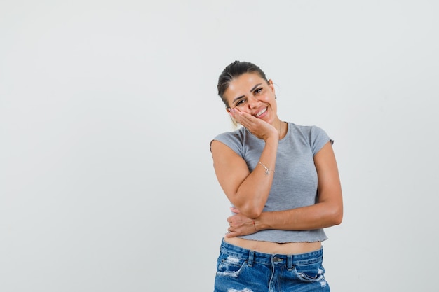 Tシャツを着た若い女性、上げられた手のひらに頬をもたれ、かわいく見えるショーツ