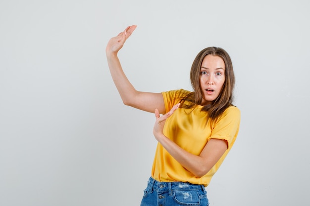 Young female in t-shirt, shorts showing stop gesture and looking scared