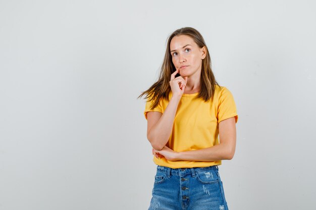 Young female in t-shirt, shorts thinking with finger on chin and looking confused