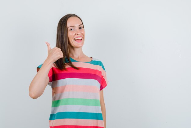 Молодая женщина в футболке показывает палец вверх и выглядит счастливым, вид спереди.