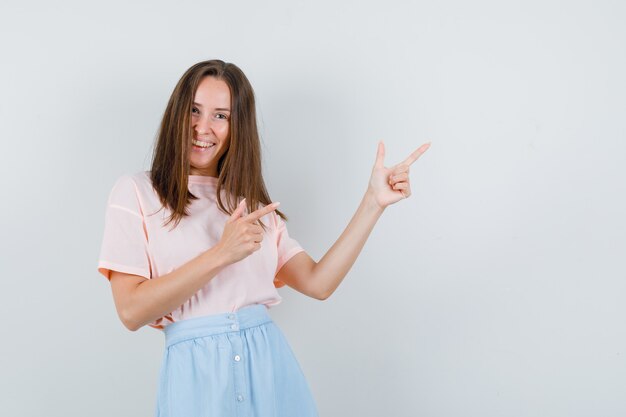 Young female in t-shirt, skirt showing gun gesture and looking cheerful , front view.