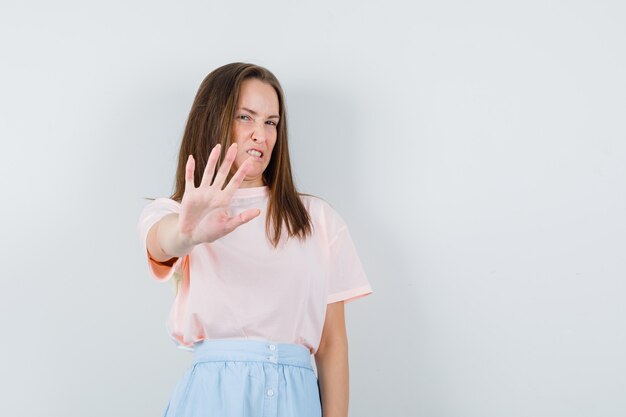 Молодая женщина в футболке, юбка показывает жест отказа и выглядит раздраженной, вид спереди.