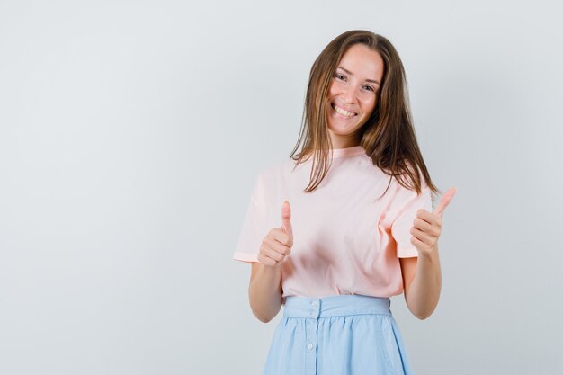 Tシャツを着た若い女性、親指を立てて幸運に見えるスカート、正面図。