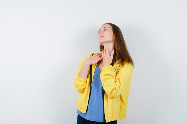 Young female in t-shirt touching skin on her neck and looking delicate, front view.