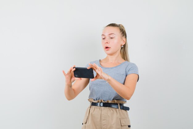 T- 셔츠, 바지, 전면보기에서 휴대 전화에 젊은 여성 복용 사진.
