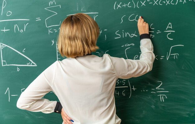 교실에서 보드 좌초와 칠판에 뭔가 쓰는 칠판 앞에 서있는 젊은 여성 교사