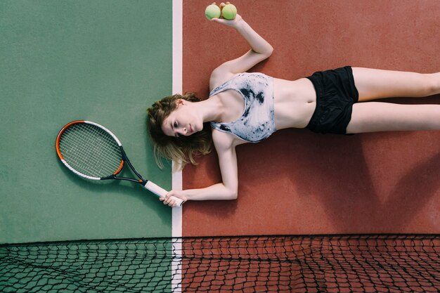 Young female tennis player lying on ground