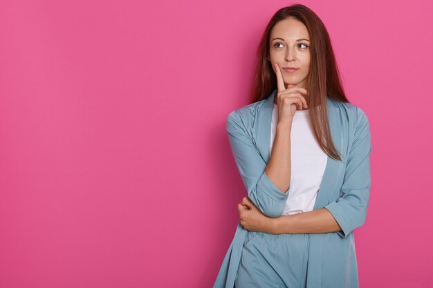 Young female thinking and pondering over something with her finger on her chin, looking aside with pensive facial expression