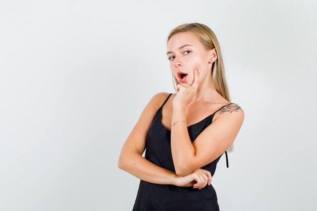 Young female thinking with finger on cheek in black singlet 