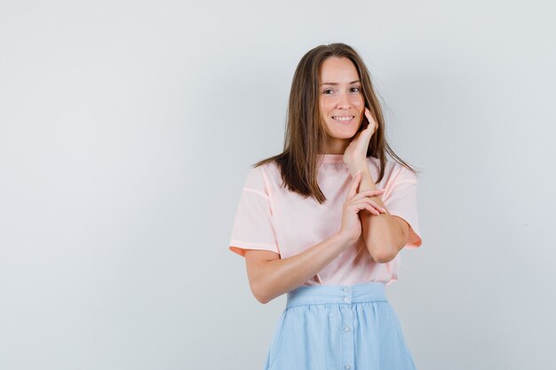 Young female touching cheek in shirt, skirt and looking cute , front view.