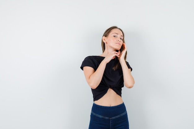 Young female touching cheek with fingers in black blouse, pants and looking confident.